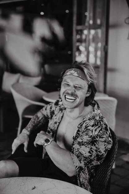 Young handsome hippie man in a red bandana, with a naked torso in a cafe in Bali. Happy man smiling