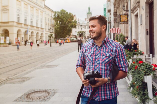 旧市街の通りを写真カメラで歩く若いハンサムな流行に敏感な男