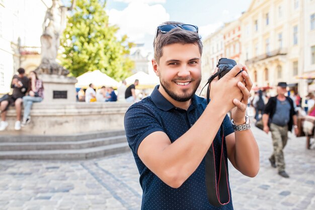 旧市街の通りを写真カメラで歩く若いハンサムな流行に敏感な男