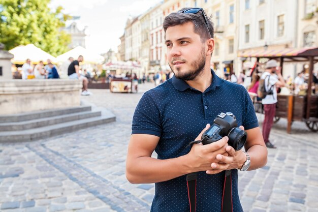 旧市街の通りを写真カメラで歩く若いハンサムな流行に敏感な男