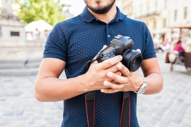 旧市街の通りを写真カメラで歩く若いハンサムな流行に敏感な男