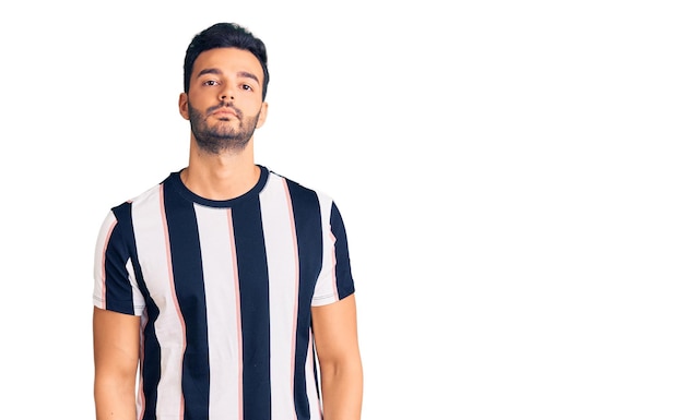Young handsome hispanic man wearing striped tshirt relaxed with serious expression on face. simple and natural looking at the camera.