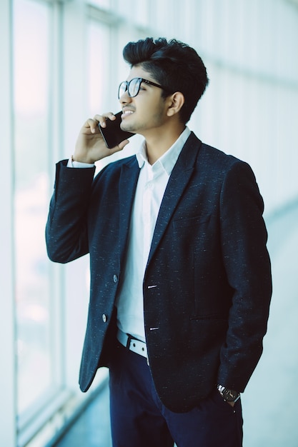 Young handsome indian businessman talking on mobile phone in modern office