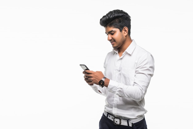 Young handsome Indian man using mobile phone isoated on white wall