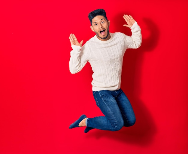 Young handsome latin man wearing casual clothes smiling happy Jumping with smile on face over isolated red background