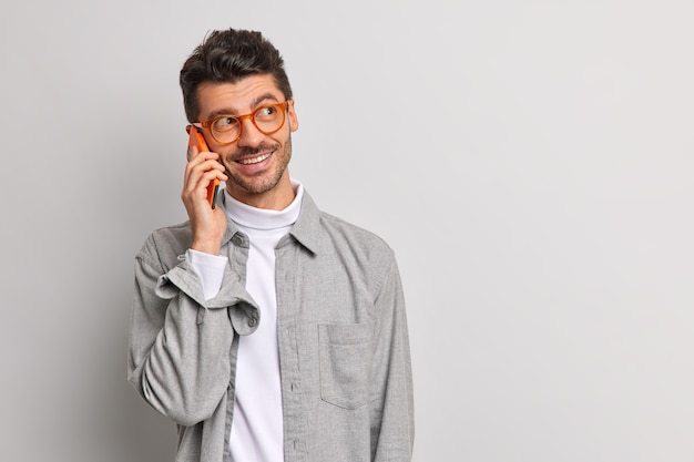 Бесплатное фото Молодой красивый мужчина-фрилансер разговаривает по мобильному телефону с веселым выражением лица, пользуется мобильными тарифами и подключением