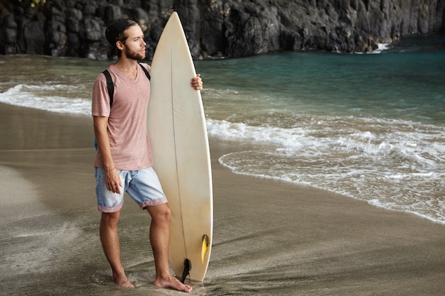 이국적인 해변에서 서핑 보드와 함께 포즈 젊은 잘 생긴 남성 모델
