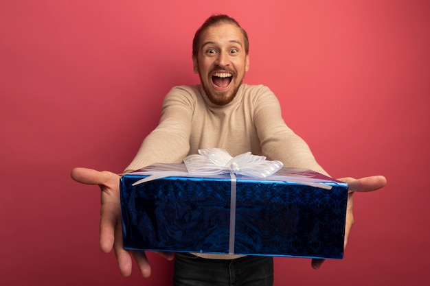 Free photo young handsome man in beige turtleneck showing gift box crazy happy