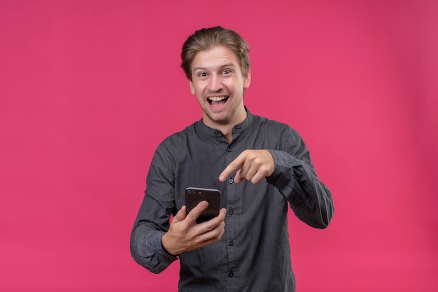 Young handsome man in black shirt holding mobile phone pointing with finger to it