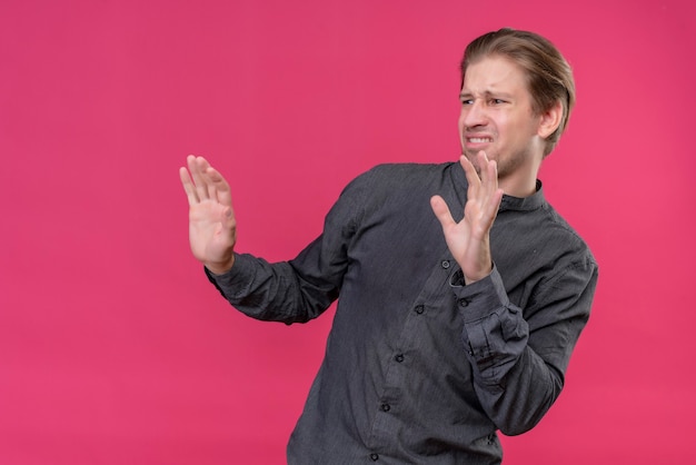 Young handsome man in black shirt raising palms holding his hands up telling do not come closer