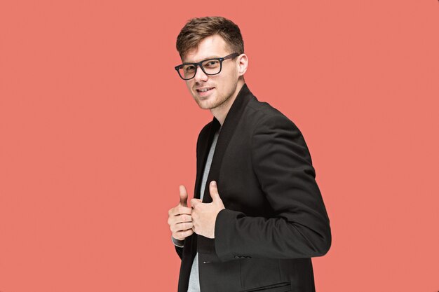 Young handsome man in black suit and glasses isolated on red wall