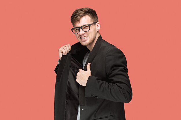 Young handsome man in black suit and glasses isolated on red