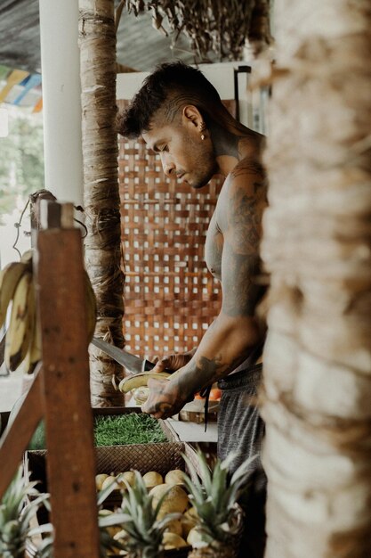 Young handsome man body in tattoos chooses fruits in the store, bananas.