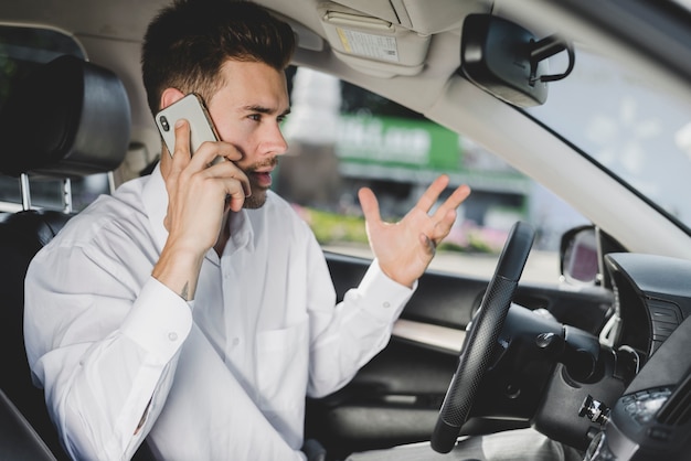 Young handsome man in car talking on mobile phone gesturing