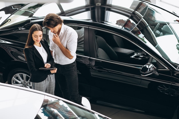 Foto gratuita giovane uomo bello che sceglie un'automobile in una sala d'esposizione dell'automobile