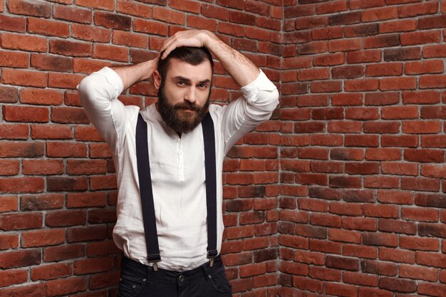 Young handsome man correcting hairstyle on brick wall.