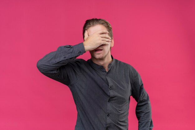 Young handsome man covering eyes with his hand standing over pink wall