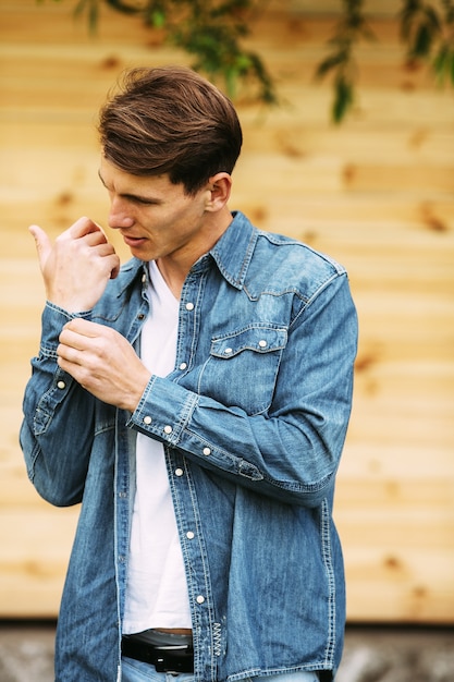 Free photo young handsome man in a denim shirt posing against a wooden wall