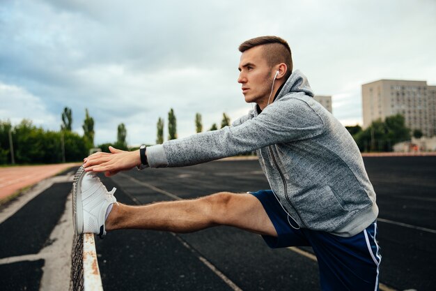 young handsome man doing exercises, working out legs, listening to music