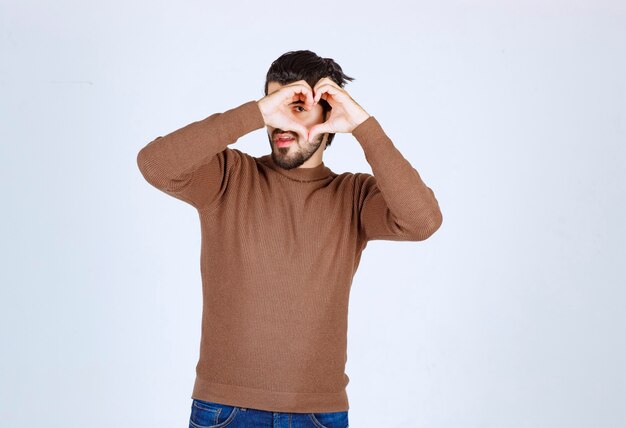 Young handsome man doing heart symbol shape with hands.