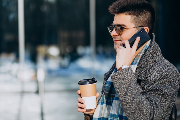 Young handsome man drinking coffee outside and using phone