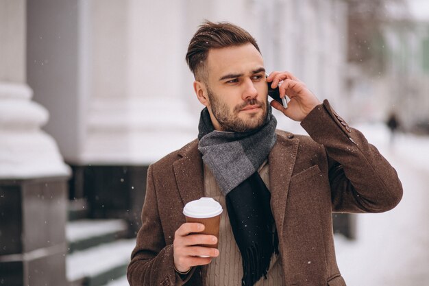 Молодой красивый мужчина пьет кофе и разговаривает по телефону