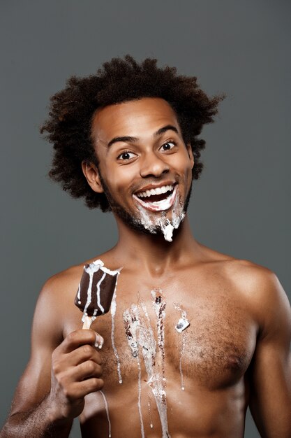 Young handsome man eating icecream over grey wall