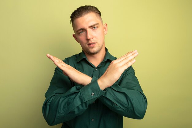 Young handsome man in green shirt making stop gesture crossing hands with serious face 