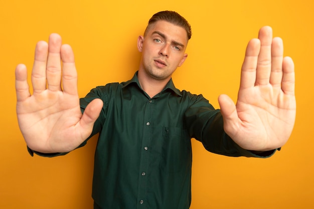 Young handsome man in green shirt making stop gesture with open hands with serious face 