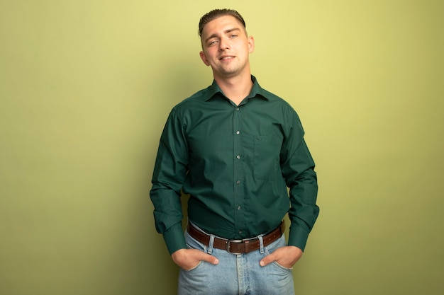 Giovane uomo bello in camicia verde che sorride fiducioso tenendo la mano in tasca