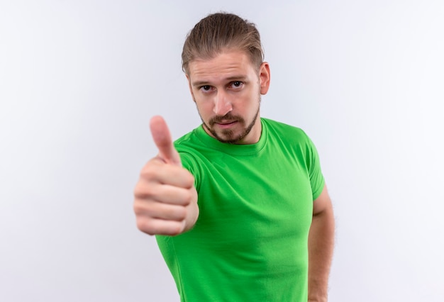 Young handsome man in green t-shirt looking at camera with confident expression showing thumbs up standing over white background