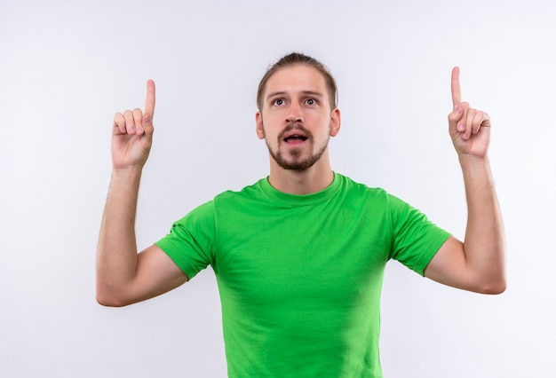 Young handsome man in green t-shirt pointing fingers up looking confident having great idea standing over white background