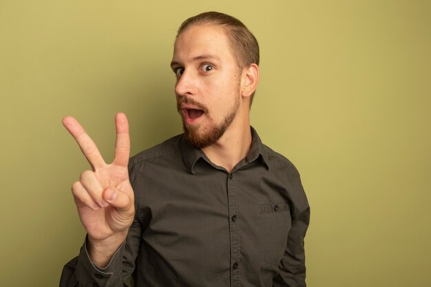 Young handsome man in grey shirt happy and excited smiling confident showing v-sign 