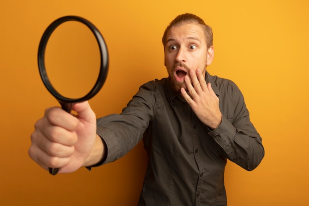 Free photo young handsome man in grey shirt holding magnifying glass looking at it amazed and surprised