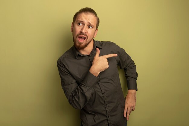 Young handsome man in grey shirt looking aside confused pointing with index finger to the side 