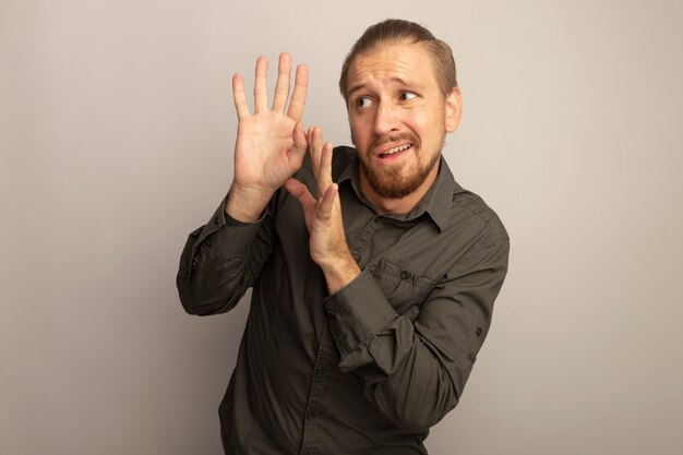 Young handsome man in grey shirt looking aside worried makin defense gesture with hands 