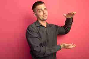 Free photo young handsome man in grey shirt looking at front smiling confident showing size gesture with hands measure symbol standing over pink wall