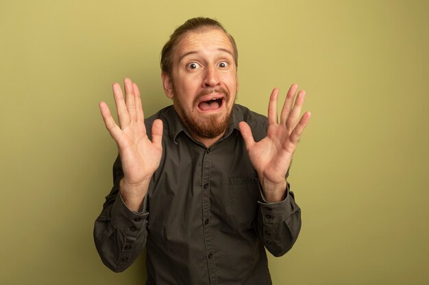 Young handsome man in grey shirt scared with raised hands 