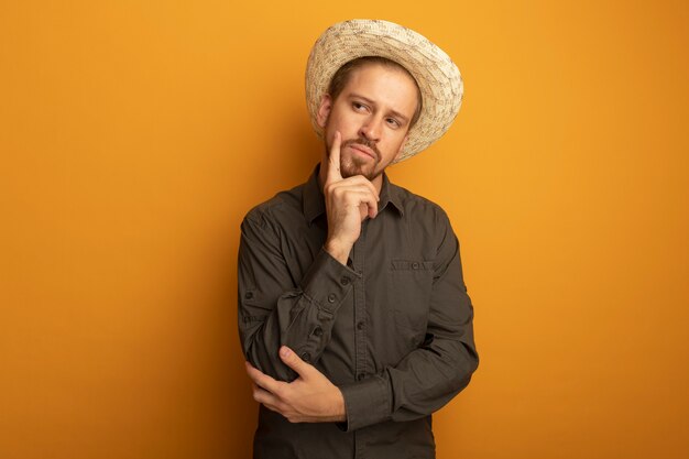 Young handsome man in grey shirt and summer hat looking aside puzzled 