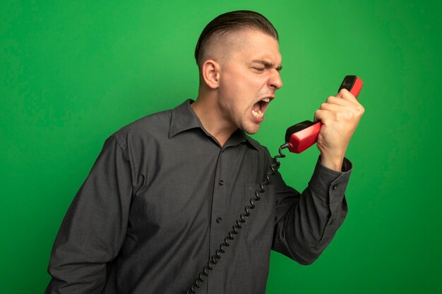 Young handsome man in grey shirt talking on vintage phone shouting and yelling frustrated 