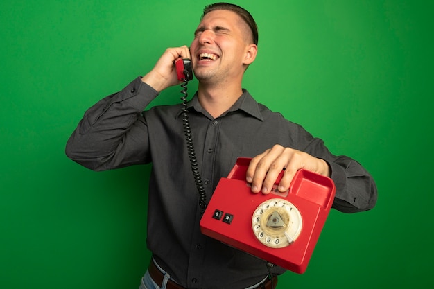 Free photo young handsome man in grey shirt talking on vintage phone smiling cheerfully standing over green wall