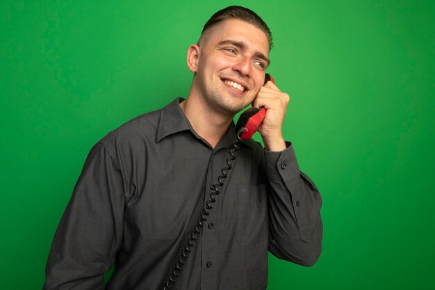 Young handsome man in grey shirt talking on vintage phone smiling cheerfully 