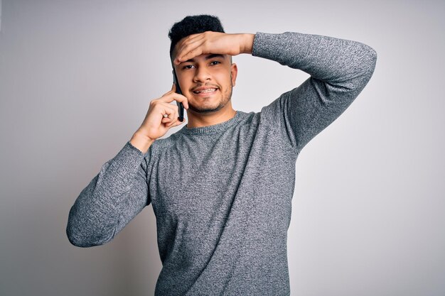 Young handsome man having conversation talking on the smartphone over white background stressed with hand on head shocked with shame and surprise face angry and frustrated Fear and upset for mistake