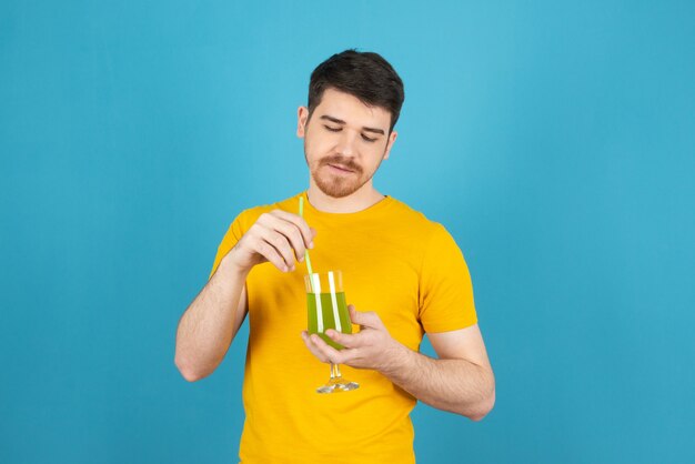 Young handsome man holding fresh cocktail and mixing it .