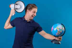 Free photo young handsome man holding globe and megaphone looking playful and happy standing over blue background