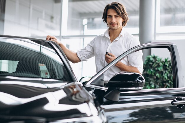 Young handsome man holding keys in a car showroom