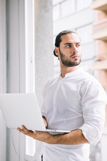 Young handsome man holding laptop device in hand looking away