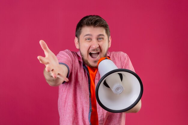 Young handsome man holding megaphone shouting to it standing with raised hand