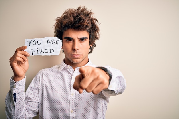 Giovane uomo bello che tiene la carta con un messaggio in piedi su sfondo bianco isolato che punta con il dito verso la fotocamera e ti fa segno con la mano gesto positivo e fiducioso dalla parte anteriore