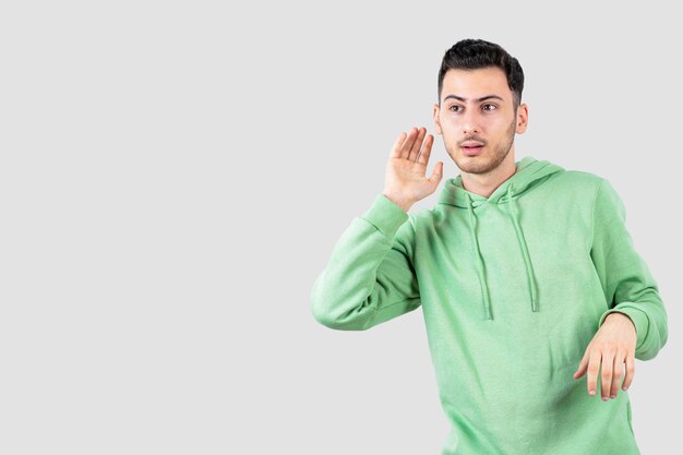 young handsome man in hoodie standing and trying to hear something